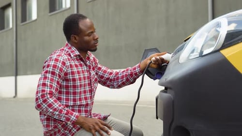Young Adult Charging Electric Car in the City