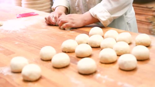 Woman breadmaker employee in the artisan bakery workshop preparing the dough in a circle