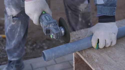 Man Cuts Plastic Pipe with Grinder on Wood Surface