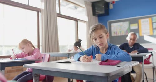 In school, girl writing in notebook while concentrating in classroom