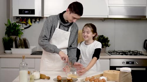 Niño y niña baten huevos batiendo huevos con batidora de mano en un tazón transparente sobre la mesa Happy Brother y
