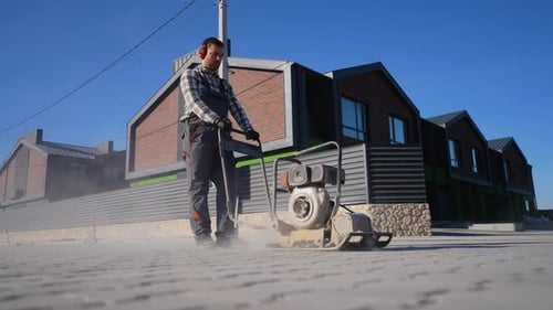 Man Using Mechanical Plate Compactor in Urban Area