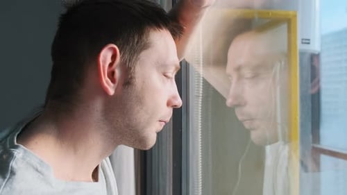 Sad Man Looking Through Window with Reflection Feeling Loneliness and Depression at Home Thoughtful