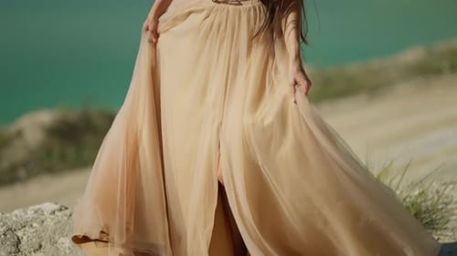 Elegante mujer vestida de color beige disfruta de la serenidad junto a un lago turquesa con su largo cabello ondeando en el viento