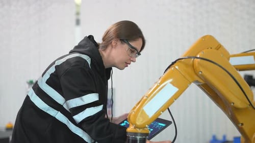 Une
technicienne programme un bras robotique avec une tablette numérique et un robot d'assemblage dans une usine. Appren
