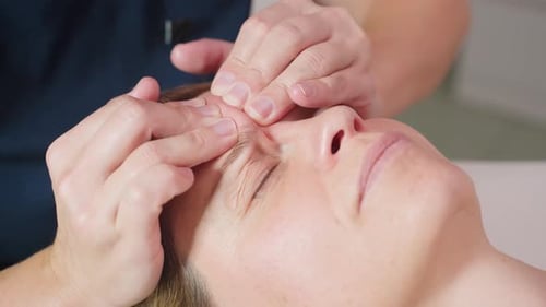 Facialist Massaging Client Forehead Brow for Tension Release Under Spa Lighting