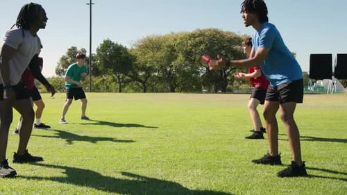 Diverse male teammates tossing red rubber ball and practicing catch drill on field