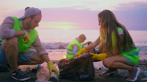 eine positive Gruppe von Freiwilligen, die bei Sonnenuntergang die Küste vom Plastikmüll säubern