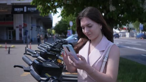 a Woman in the City Using a Smartphone and an Application is Trying to Rent a Scooter for Movement