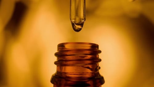 Dropper Dripping Golden Substance into Brown Bottle