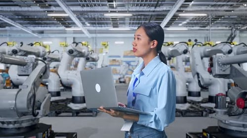 Woman Using Laptop with Robotic Arms in Factory
