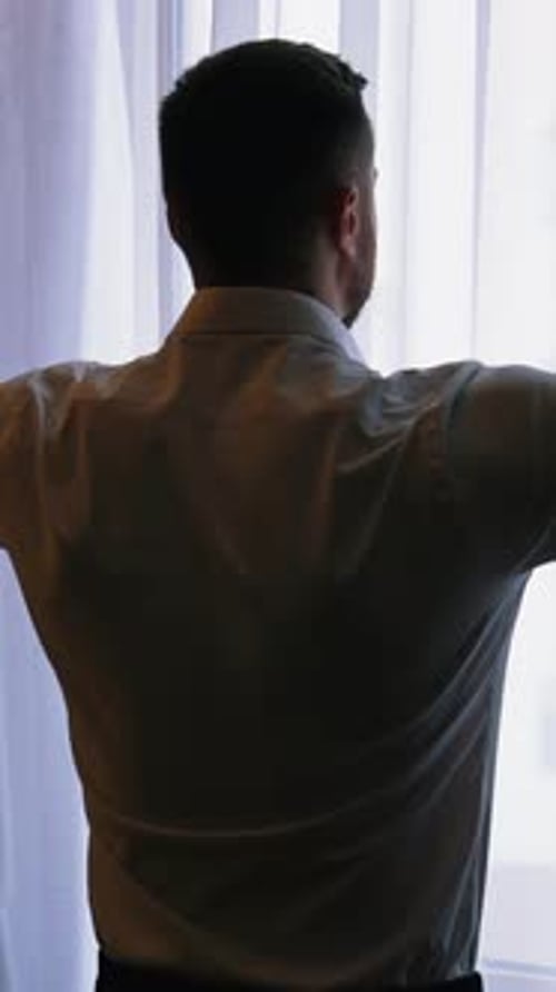 Junger Mann öffnet Gardinen im Hotelzimmer.