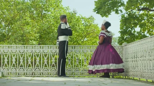 Couple in Historical Costumes Talking on Outdoor Terrace Overlooking Garden