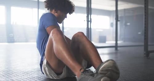 Exercising in gym, man doing sit-ups with medicine ball, focusing on fitness