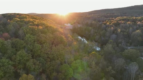 River stream between colored trees in autumn. Aerial wide shot. Sunset time behind mountains of