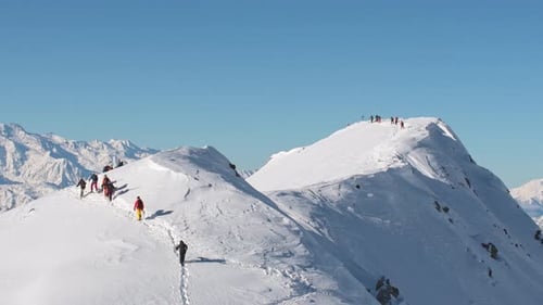 People Climbing Snowy Mountain Peak on Sunny Day