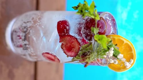 Mojito cocktail glass with ice and cherry and mint, soda and gin near a blue pool close up