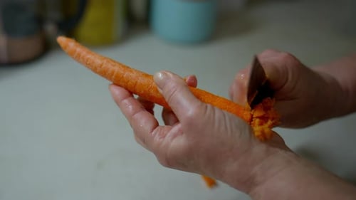 Pelando zanahorias frescas a mano con un pelador de verduras en la cocina