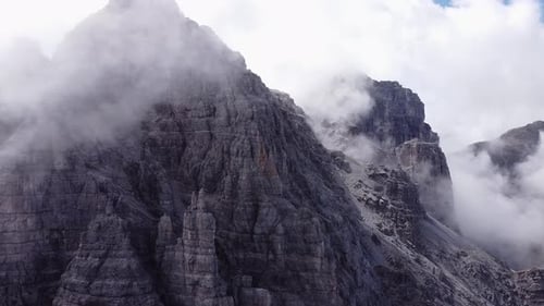 Aerial of steep rocky alpine mountain ranges, foggy clouds around peak, epic landscape drone scenery