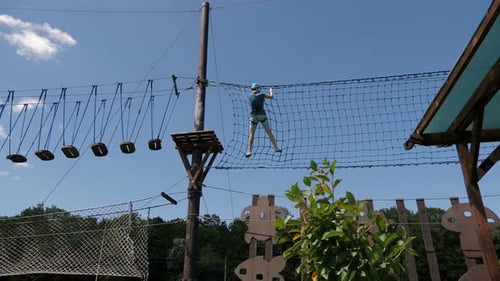 A Woman Walks Along the Path of a Rope Park High Above the Ground