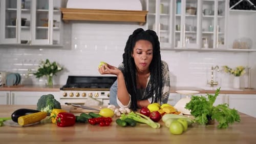 Woman Eats Apple Surrounded by Fresh Vegetables