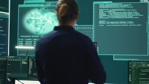 Male Programmer Stands Before Wall of Code Monitors