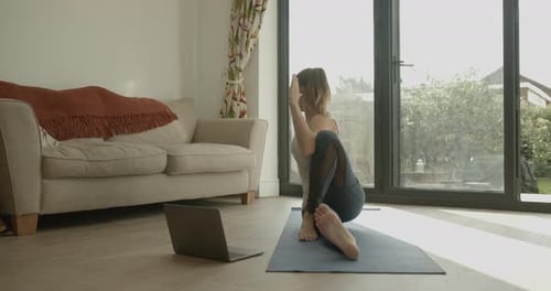 Mujer practicando ejercicios de yoga en casa viendo un vídeo tutorial en un ordenador portátil durante el encierro