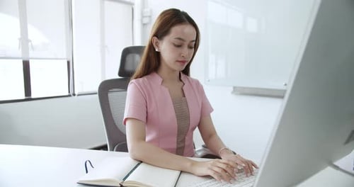 A young woman diligently types at her computer in a sleek modern office space.
