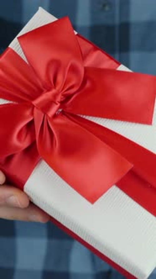 Man shows gift box with tied red bow for St. Valentine's Day. Vertical video