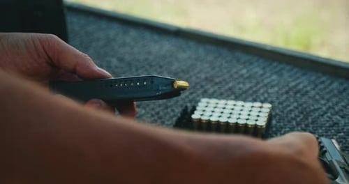 Hands Loading Bullets into Pistol Magazine at Gun Range