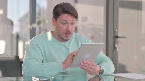 Man Celebrates Success Using Tablet at Desk