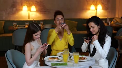 Smiling Pretty Ladies Sitting in the Restaurant While Holding Smartphones and Making Photos of Food