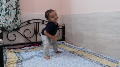 cute toddler baby boy trying to stand for the first time at bed at home
