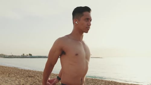 Young athletic man standing on the beach doing muscle stretching before training