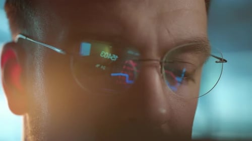 Trader Wearing Glasses is Working on Laptop Computer Screen with Stock Market Charts and Bitcoin BTC