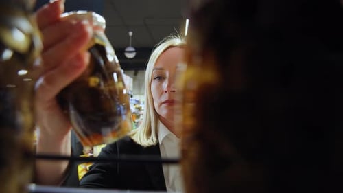 Woman Comparing Jarred Vegetables on Supermarket Shelf