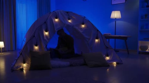 Child Reads Inside Cozy Blanket Fort at Night