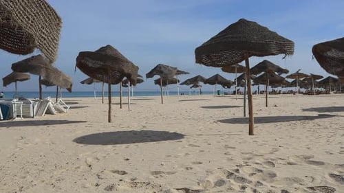Empty beach with woven parasols casting shadows on the sand by the Mediterranean Sea
