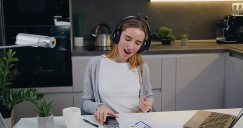 Mujer feliz y relajada bailando sentada en el ordenador portátil con auriculares escuchando música