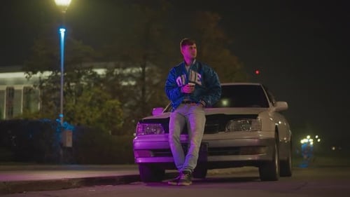 Young Man Leans on Car at Night with Coffee