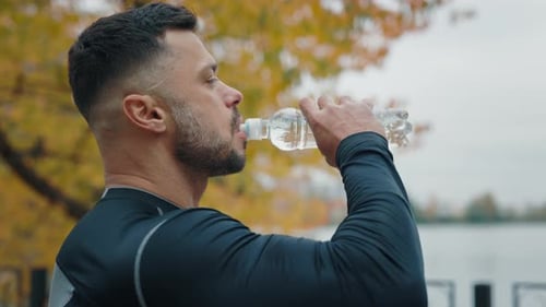 Side View of the Man Jogger Drinking Water After Exercising Mature Male Drinks Refreshing Water From