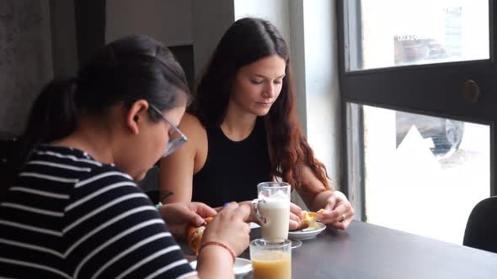 Young women sharing coffee, pastries, and laughter while seated at cafe ...