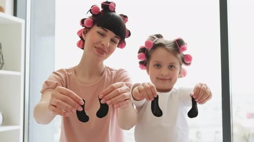 Mother and Daughter with Hair Rollers Holding Eye Patches