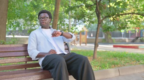 Young Man Checking Watch while Sitting on Bench