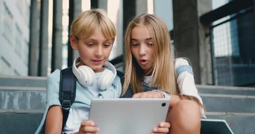 Two school children pupils girl and boy classmates friends sitting on stairs street outdoors