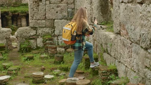 A young female traveler with a backpack explores the ruins of an ancient Greek city and takes photos