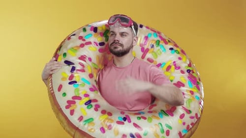 A Playful Man with a Donut Float on a Bright Yellow Background During Summer Days