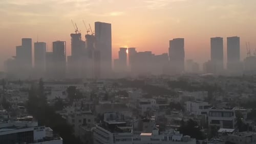 Aerial View Of Buildings In City Against Orange Sky During Foggy Weather, Drone Flying Upwards Over