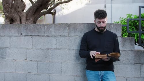 Man Reads Old Book Leaning Against Wall