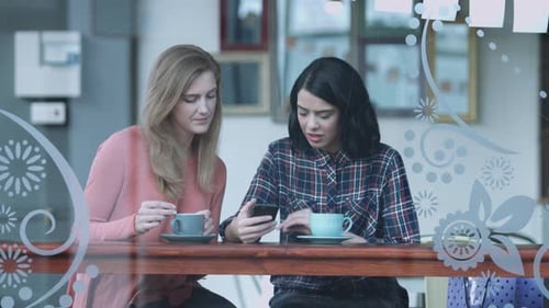 Female friends in coffee shop looking at smart phone